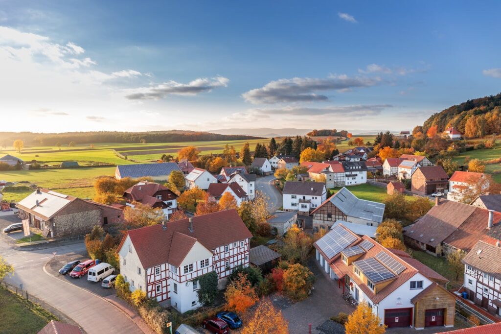 Idyllisches Dorf in herbstlicher Landschaft mit Fachwerkhäusern und grünen Feldern unter blauem Himmel