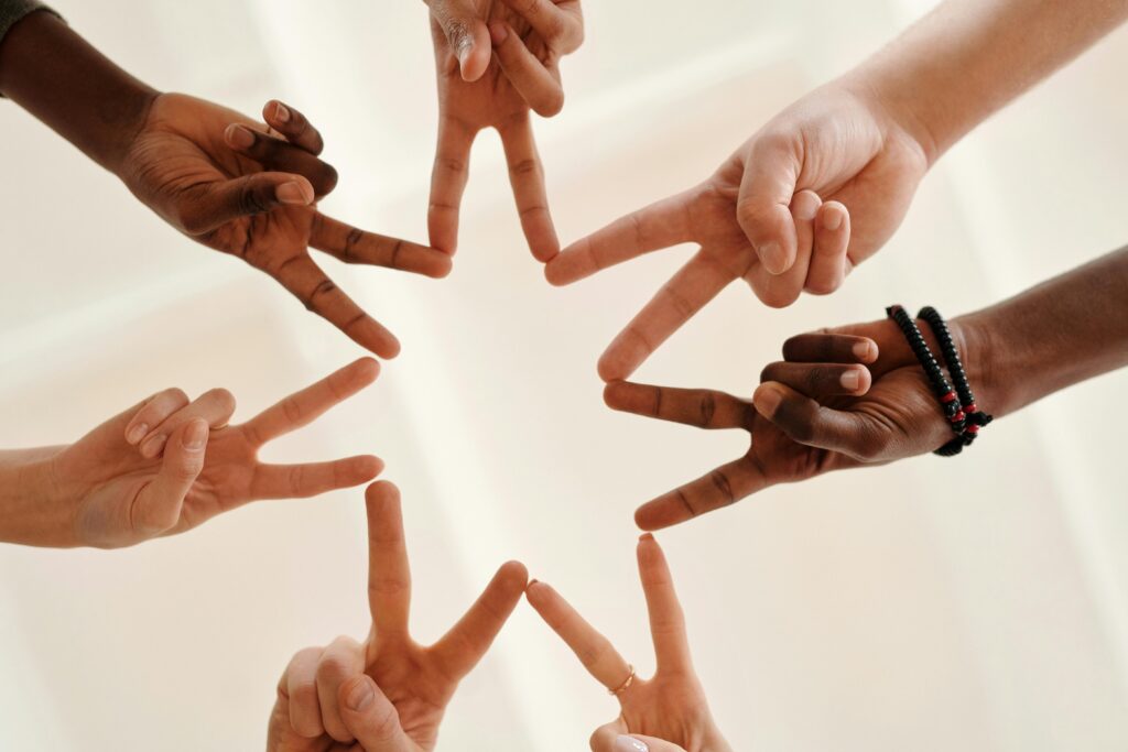 Mehrere Hände bilden durch ausgetreckte Zeige und Mittelfinger einen Stern und zeigen so Teamwork, Verbindung und Vereinigung.