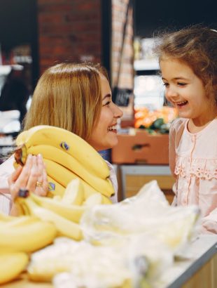 Mutter und Tochter beim einkaufen Lächelnde Mutter zeigt ihrer Tochter Bananen in der Obstabteilung eines Supermarkts