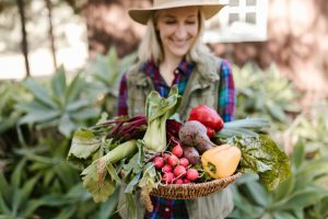 pexels-photo-7782981-7782981 Smiling woman holding fresh farm produce in a basket outdoors, showcasing colorful vegetables.